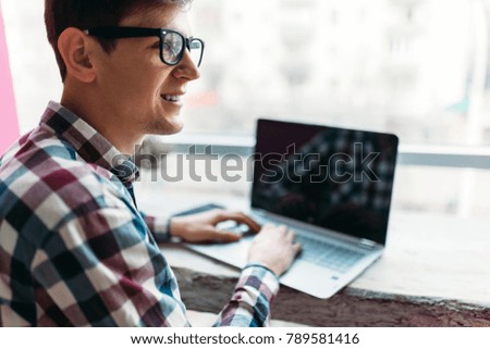 A young man sits in a cafe with a laptop, search the Internet, typing on laptop, a man in a checkered shirt on