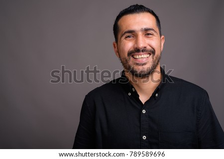 Studio shot of handsome bearded Persian man wearing black shirt against gray background Royalty-Free Stock Photo #789589696