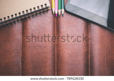 Digital pad and supplies on brown leather background with copy space. Top view. Technology concept. Mock up 