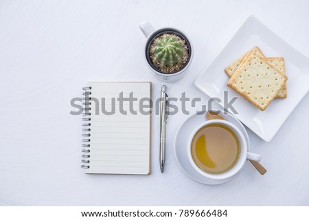 Blank notebook with hot tea and biscuit on white table background, tea break time