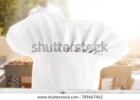 White cook hat on white wooden table and cook chef background with grill 