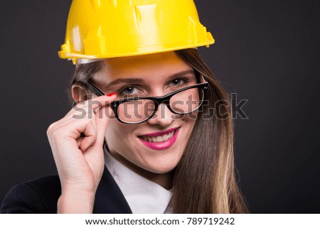 Beautiful young architect woman with yellow helmet smiling and looking confident over her glasses