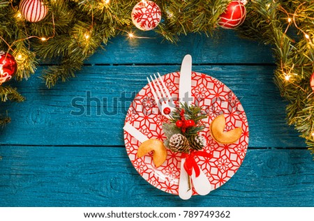 Photo of pine branches, plates with red pattern, prediction cookies, fork, knife, Christmas decoration