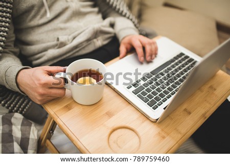 Young man laying in bad with laptop and cup of tea.