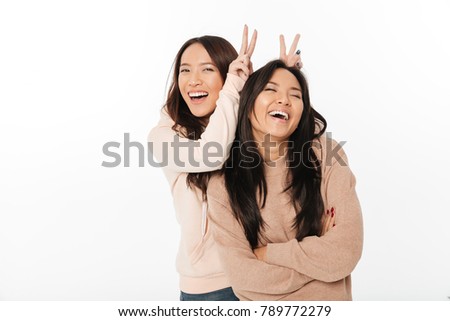Picture of two asian cute ladies sisters standing isolated over white background looking camera have fun.