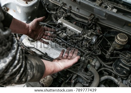 A picture of dirty hands of a guy above the engine from the garage. Hard and dirty work is behind him. 