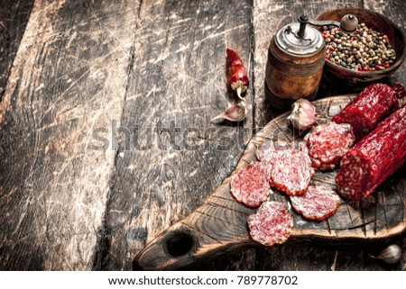 salami with herbs and spices on a board. On a wooden background.