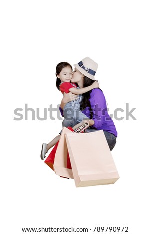 Portrait of young woman carrying shopping bags while kissing her daughter, isolated on white background