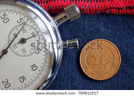 Euro coin with a denomination of 5 euro cents (back side) and stopwatch on worn blue jeans with red stripe backdrop - business background