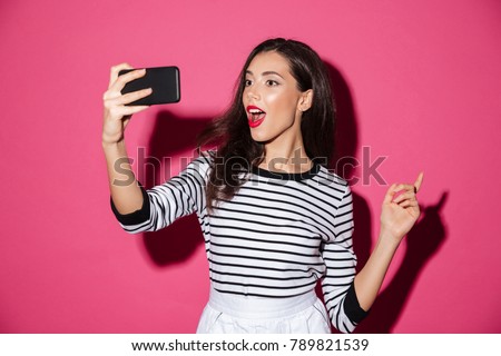 Portrait of a pretty girl taking a selfie isolated over pink background