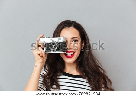 Close up portrait of a pretty woman taking a photo with a vintage camera isolated over gray background