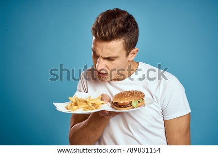  a man looks at fast food on a blue background, harmful, hungry                              