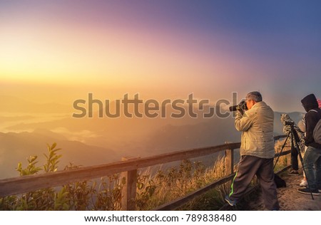 Old asian photographer stand taking photo sunrise view on high angle viewpoint top of the mountains in early morning