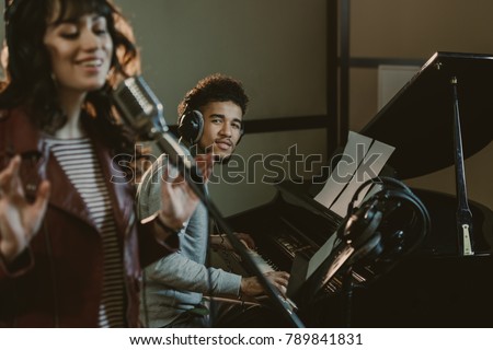 young handsome piano player looking at singer performing song