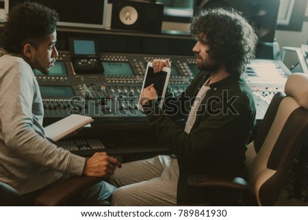 man showing blank tablet screen to sound producer at recording studio