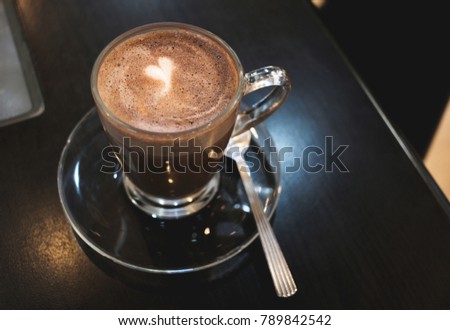 Brown cocoa in coffee cup with white heart shape on black wooden table background. Valentine's day and love concept