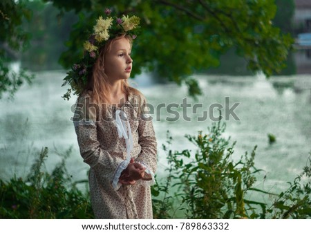 A blonde girl in the traditional slave dress launching a flower wreath with a candle in the river. Russian pagan traditional holiday Ivan Kupalo