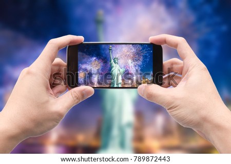 Traveler holding smartphone to take a photo of The Statue of Liberty and cityscape with beautiful fireworks at night, Manhattan, New York City, USA