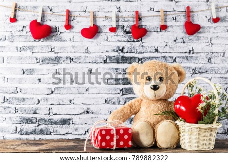 A photo of teddy bear sitting near red gift box with white brick wall background, Valentine concept