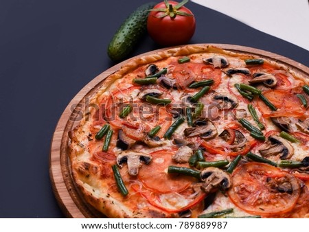 Pizza with tomatos, champignons, green beans and cheese on a dark blue/black  background.