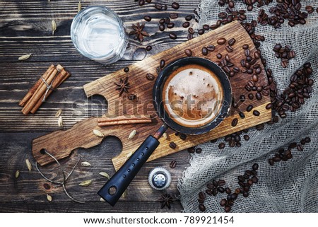 
coffee in cezve on a rustic wooden table with spices, cinnamon, water, salt and coffee beans near the window. Royalty-Free Stock Photo #789921454