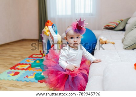 Cute girl child in pink skirt posing near sofa in spacious room