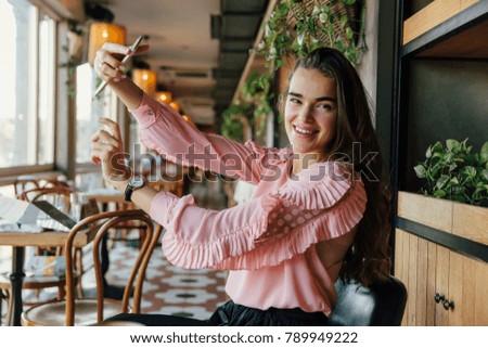 Beautiful long-haired brunette girl doing selfie at a cafe. Photographed, fooled and fun. Pretty mixed race girl photographing herself for sharing on social network