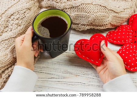 Above view of female hand holding hot cup of coffee with red heart on wood table. Photo in vintage color image style.