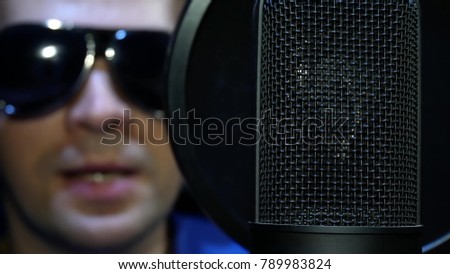 Blind Man Speaks into Microphone Voices Cartoon, Movie or Promotional Movie. Blind Man in Black Glasses Reads Braille from White Paper Sheet and Recording Voice or Song in the Sound Recording Studio