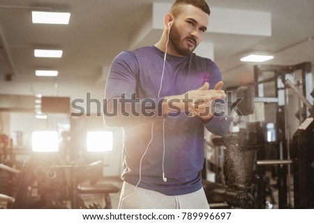 A handsome young man athlete trains in the gym. Handsome weightlifter preparing for training.  Hands in chalk. male powerlifter hand in talc 
