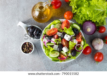 Fresh Greek salad made of cherry tomato, ruccola, arugula, feta, olives, cucumbers, onion and spices. Caesar salad in a white  bowl on wooden background. Healthy organic diet food concept. 