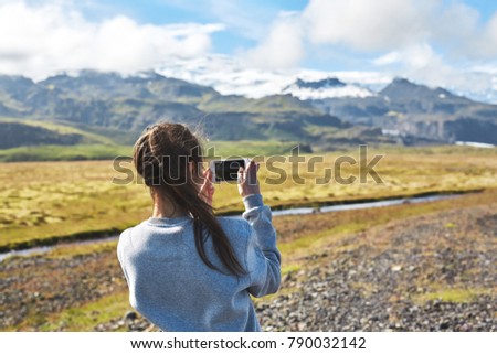 back view of woman tourist on the snow cupped Vatna volcano background in Iceland. Travel to Iceland. woman taking photo on phone