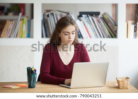 Young focused female student working on laptop sitting at home office desk, serious businesswoman entrepreneur using computer, concentrated woman online business owner typing on pc at workplace