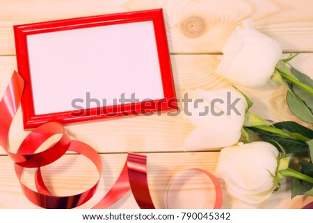 Concept of Valentine's Day with beautiful white roses and red photo frame natural wooden background top view