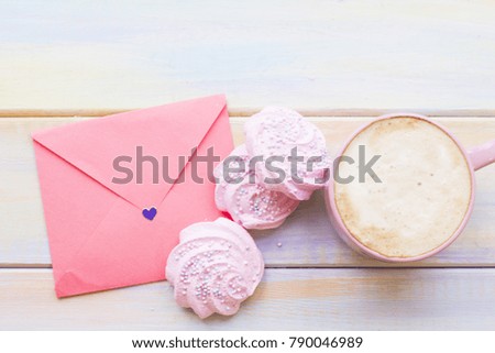 A light colored wooden background with a cup of hot coffee, pink marshmellows and an envelope. St.Valentine's, wedding, anniversary concept. Space for a text or product display