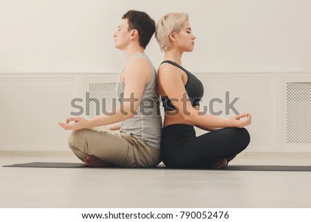 Young couple meditating together. Man and woman sitting back to back in lotus pose on mat, copy space