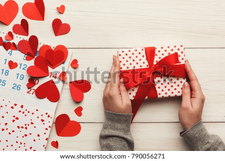 Valentine background with red paper hearts border and gift box in female hands, copy space on white rustic wood. Happy lovers day present mockup