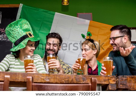 Four good friend talking and drinking beer in pub with Irish flag on background and smile