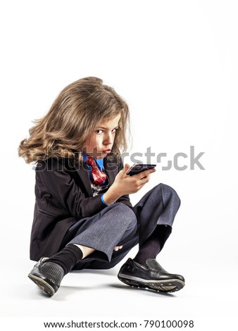 Little smiling boy in the clothes of a businessman playing games or surfing internet on digital smartphone. White background.
