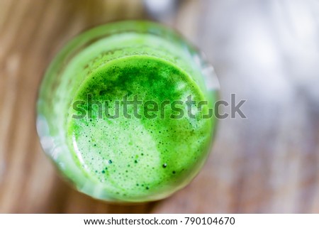 Macro closeup flat top view of bubble surface of green juice smoothie in glass with wooden background