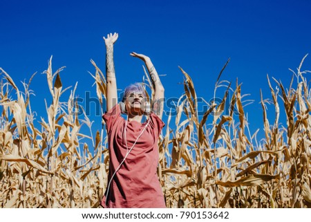 
Young tattooed woman dancing while listening to music with her headphones. Dance free and happy in front of a wheat field on a sunny day. Lifestyle