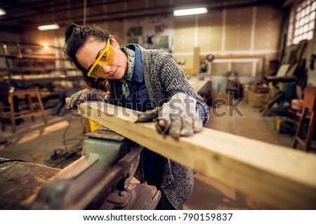 Portrait view of happy attractive hardworking middle aged professional female carpenter worker looking and choosing wood in the workshop or garage. Royalty-Free Stock Photo #790159837
