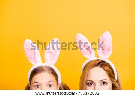 Cropped close up half-faced portrait photo of excited cheerful beautiful mom and small sweet playful funny lovely tender daughter wearing bunny ears isolated on yellow background