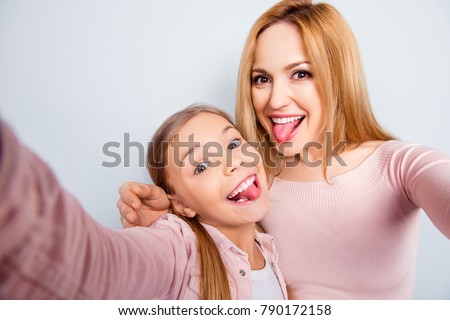 Self portrait of crazy, foolish mother and doughter showing tongue out, kid making selfie on mobile phone over grey background, spending weekend, woman's day together Royalty-Free Stock Photo #790172158