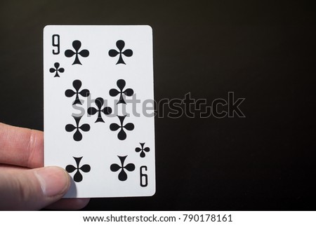 Man hand holding playing cards nine of clubs isolated on black background with copyspace