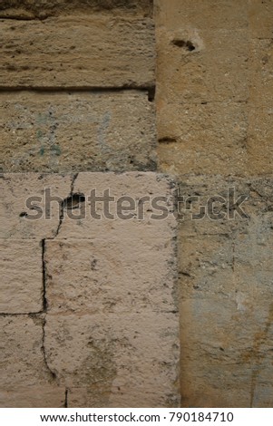 Detail of the texture of a dark mediterranean wall colored in grey, brown and beige. The surface is rough, made of old stones and rocks. Holes, lines and patches can be seen and compose the pattern. 
