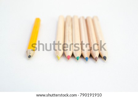 Six wood colored crayons on white background and a single grey one.