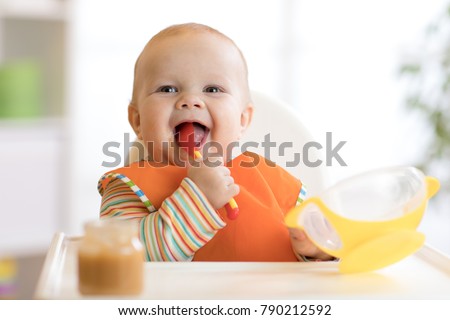 Happy infant baby boy spoon eats itself at home Royalty-Free Stock Photo #790212592