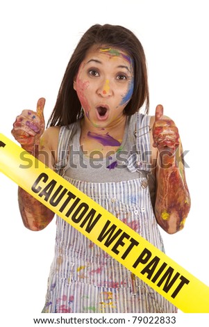 A woman covered in paint with her thumbs up at the wet paint sign.