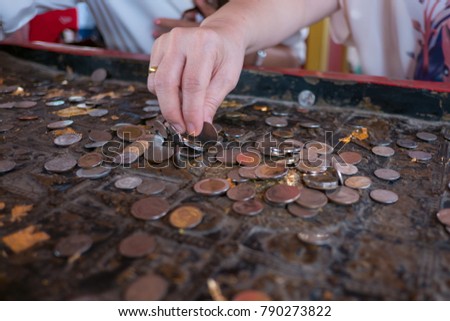 Close up of hands trying to set a coin balance on its edge on Buddha footprint, Thailand. It believe that good fortune will come.